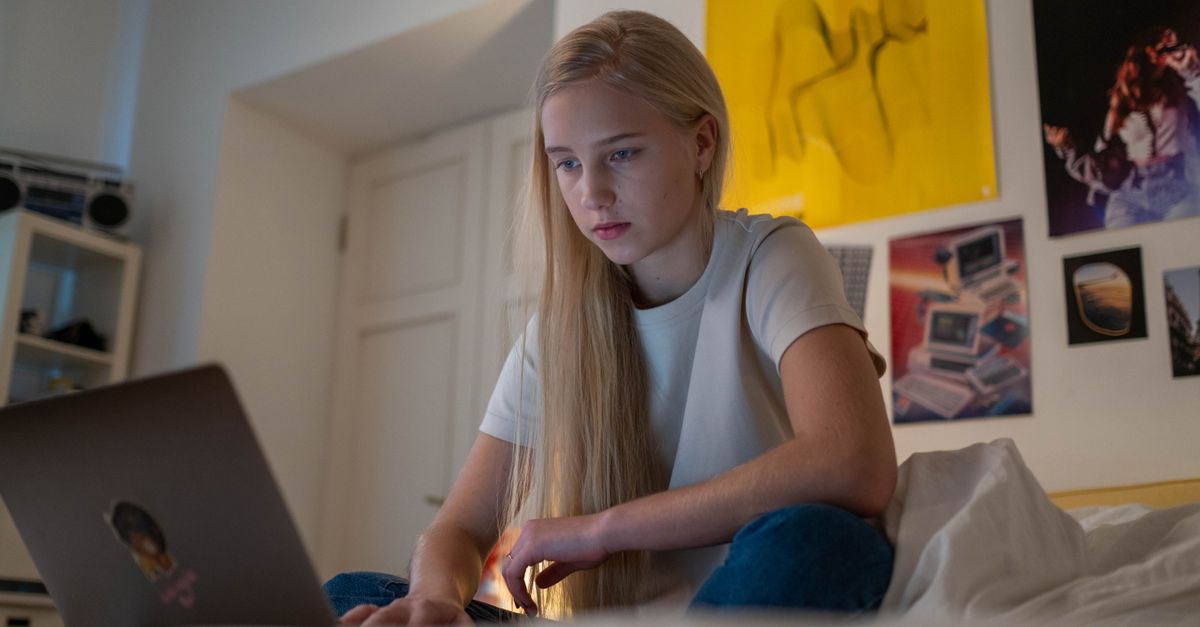 dimly lit teenage bedroom with a girl filming herself, a cheap laptop on a desk, and a futuristic robot on a track