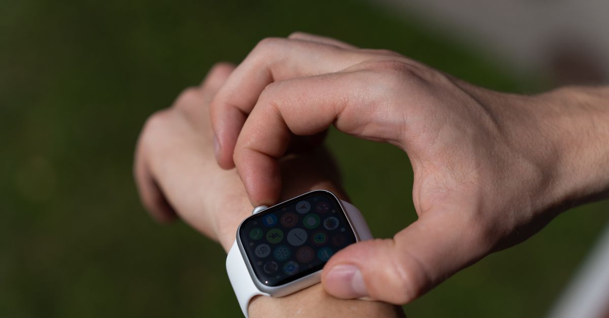 a backyard patio with a sleek mosquito repellent device, a minimalist Mac laptop displaying a plain text task list, a smartwatch on a wrist showing health metrics, a bird feeder with a small camera