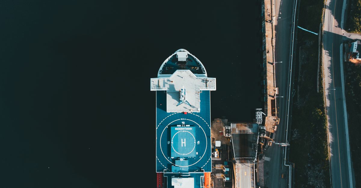 cargo ship burning beside a corporate skyscraper with streaming logos and drones overhead