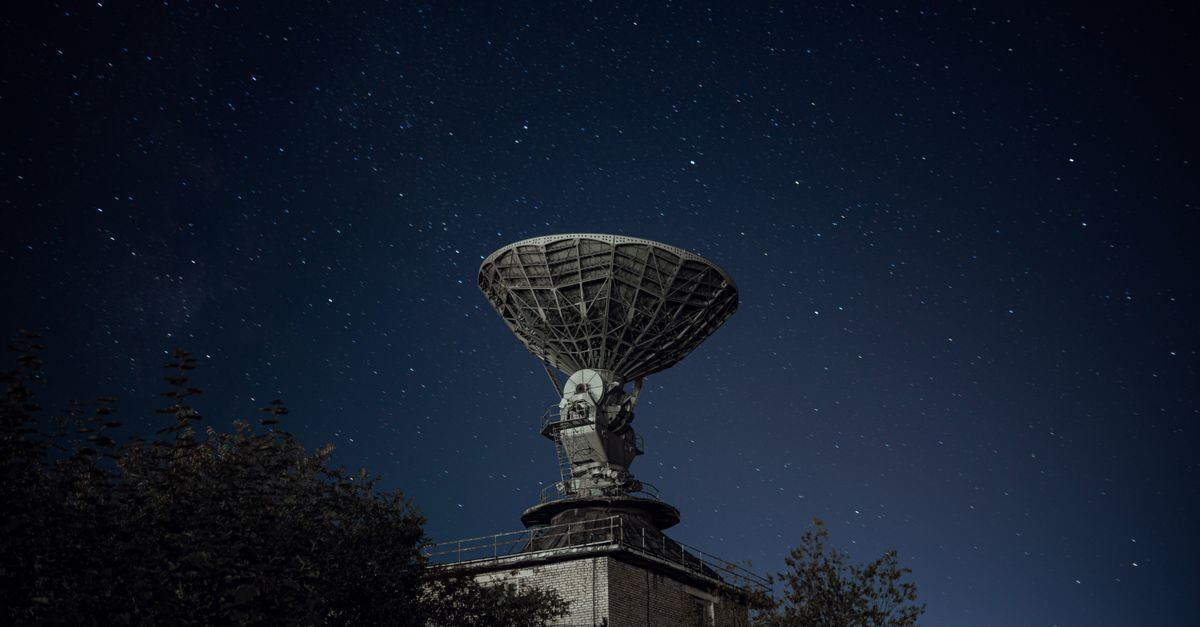satellite dish illuminated against night sky over war‑torn city